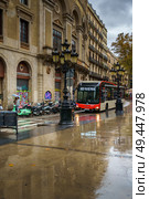 Barcelona, Spain - Nov 9 2018, Vertical view of La Rambla street where the bus is driving, in rainy weather with a wet sidewalk, without people, at daytime, Barcelona, Spain. Редакционное фото, фотограф Сергей Богомяко / Фотобанк Лори