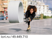 Young fit black woman on roller skates riding outdoors on urban street. Smiling girl with afro hairstyle rollerblading on sunny day. Black woman on roller skates riding outdoors on urban street. Стоковое фото, агентство Ingram Publishing / Фотобанк Лори