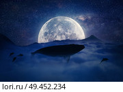 Silhouette of a whale flying above the clouds into the full moon night. Starry sky over the clouds in the mountains. Fantasy, surreal landscape scene screen saver. Стоковое фото, агентство Ingram Publishing / Фотобанк Лори