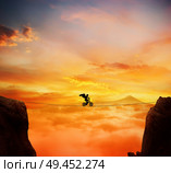 Boy with angel wings balance on a rope over a chasm riding a bicycle.Self overcoming and risk taking concept. Beautiful sunset background over the clouds. Стоковое фото, агентство Ingram Publishing / Фотобанк Лори