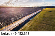 Spring green and black agricultural fields. Asphalt rural road. Melting snow in march. Lone tree on a road side. Winter crops and plowed field. Spring countryside aerial landscape. Belarus . Стоковое фото, агентство Ingram Publishing / Фотобанк Лори