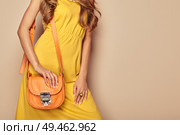Portrait of Fashion Young Woman in Yellow Dress. Female Model in Stylish Spring Summer Outfit. Girl Posing on a Beige Background. Stylish Hairstyle. Blonde Lady with Orange Handbag. Стоковое фото, агентство Ingram Publishing / Фотобанк Лори