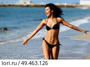 Young arabic woman with beautiful body in swimwear on a tropical beach with open arms. Brunette female smiling with curly long hairstyle wearing black bikini.. Young arabic woman with beautiful body in swimwear smiling on a tropical beach. Стоковое фото, агентство Ingram Publishing / Фотобанк Лори