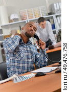 Man sat at desk, on telephone, stretching neck. Стоковое фото, агентство Ingram Publishing / Фотобанк Лори