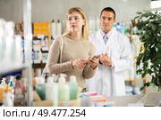 Young woman scrolling phone while looking for something and pharmacist consulting in drugstore. Стоковое фото, фотограф Яков Филимонов / Фотобанк Лори