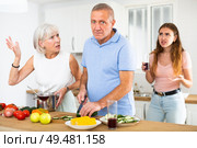An adult daughter, together with an elderly mother, scolds an elderly father while he is preparing dinner in kitchen. Стоковое фото, фотограф Яков Филимонов / Фотобанк Лори