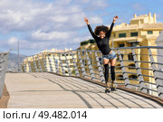 Black woman, afro hairstyle, on roller skates riding outdoors on urban bridge with open arms. Smiling young female rollerblading on sunny day. Beautiful clouds in the sky.. Afro hairstyle woman on roller skates riding outdoors on urban bridge. Стоковое фото, агентство Ingram Publishing / Фотобанк Лори