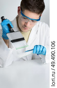 A man in a lab coat holding a multichannel pipette. Young biologist setting up PCR reaction. Стоковое фото, фотограф Аnna Ivanova / Фотобанк Лори