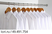 Row of neatly arranged white shirts on hangers reflecting uniformity, professionalism or fashion minimalism in workwear or retail display. Стоковое AI-изображение, AI-художник Igor Tichonow / Фотобанк Лори
