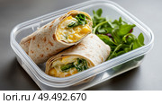 Healthy breakfast wrap with spinach and eggs in a clear container. Стоковое AI-изображение, AI-художник Katsiaryna Repich / Фотобанк Лори