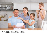Happy man with wife and teenage daughters reading notification at home. Стоковое фото, фотограф Яков Филимонов / Фотобанк Лори