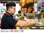 Male butcher cutting ham bones in a cutting machine inside a butcher shop.. Male butcher cutting ham bones in a cutting machine. Стоковое фото, агентство Ingram Publishing / Фотобанк Лори