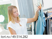 Lady in clothes shop holding top, unsure expression. Стоковое фото, агентство Ingram Publishing / Фотобанк Лори