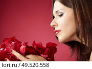Profile of the girl smelling petals of roses, isolated on a red background. Стоковое фото, агентство Ingram Publishing / Фотобанк Лори