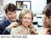 The woman tries on a necklace at a mirror in shop. Стоковое фото, агентство Ingram Publishing / Фотобанк Лори