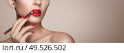 Beautiful woman paints lips with lipstick. Beautiful woman face. Makeup detail. Beauty girl with perfect skin. Red lips and nails manicure. Стоковое фото, агентство Ingram Publishing / Фотобанк Лори