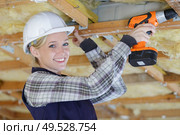 female carpenter drilling wooden roof at construction site. Стоковое фото, агентство Ingram Publishing / Фотобанк Лори