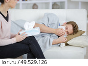 man laying on sofa blowing his nose partner holding tissues. Стоковое фото, агентство Ingram Publishing / Фотобанк Лори
