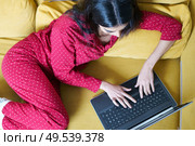 Young woman wearing pyjamas at home using laptop computer on a couch. Persian woman at home using laptop computer. Стоковое фото, агентство Ingram Publishing / Фотобанк Лори