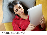 Young woman wearing pyjamas at home using digital tablet on a couch. Persian woman at home using digital tablet. Стоковое фото, агентство Ingram Publishing / Фотобанк Лори
