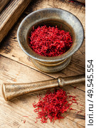 Raw organic red saffron spice on wooden background.Vintage metal mortar with pestle. Dried saffron in mortar. Стоковое фото, агентство Ingram Publishing / Фотобанк Лори