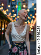 A woman with a shaved head stands confidently on a busy city street. Стоковое AI-изображение, AI-художник Данила Большаков / Фотобанк Лори