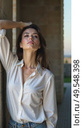 A caucasian young woman in a white blouse standing confidently with her arm scratches and ruffles her hair against a textured stone wall, soft lighting enhancing. Стоковое AI-видео, аниматор Sergey Grishin / Фотобанк Лори