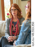 Two women engaged in conversation while sitting on a couch in a living room setting. Стоковое AI-изображение, AI-художник Данила Большаков / Фотобанк Лори