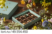 A box filled with assorted chocolates rests on a wooden table. Стоковое AI-изображение, AI-художник Данила Большаков / Фотобанк Лори