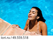 Beautiful Arab woman relaxing in swimming pool with eyes closed. Girl with healthy tanned skin and wet hair enjoying Summer Sun. Стоковое фото, агентство Ingram Publishing / Фотобанк Лори