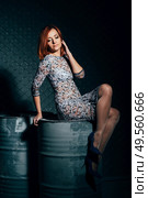 redheaded model girl in a long dress in a dark industrial Studio near barrels of oil. Стоковое фото, агентство Ingram Publishing / Фотобанк Лори