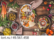 Healthy vegan food with hummus plate. Female hands holding tasty snack on kitchen tables. Ramadan iftar dinner. Various pickled and fresh  vegetables. Mediterranean cuisine. Стоковое фото, агентство Ingram Publishing / Фотобанк Лори