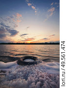 Fine art vertical shot, old vehicle tire thrown on the shore of a pond, covered with fluffy surf foam created by waves. Scenery landscape, peaceful sunset sky background over the city on the horizon. Стоковое фото, агентство Ingram Publishing / Фотобанк Лори