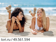 Two young women with beautiful bodies in swimwear on a tropical beach. Funny caucasian and arabic females wearing black and white swimsuits lying on the sand on the beach. Two young women with beautiful bodies in swimsuit on a tropical beach. Стоковое фото, агентство Ingram Publishing / Фотобанк Лори