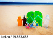 green sandals,  bottle of water and suntan creams on sandy beach by sea side, toned. sandals and  bottle of water on sandy beach. Стоковое фото, агентство Ingram Publishing / Фотобанк Лори