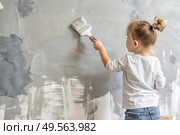 A little girl paints a wall in a new house. Interior decoration of the house, wall painting. Cosmetic repairs. Child labor. Стоковое AI-изображение, AI-художник Photojuli / Фотобанк Лори