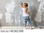 A little girl paints a wall with a paint roller in a new house. Interior decoration of the house, wall painting. Cosmetic repairs. Child labor. Стоковое AI-изображение, AI-художник Photojuli / Фотобанк Лори