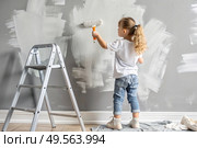 A little girl paints a wall with a paint roller in a new house. Interior decoration of the house, wall painting. Cosmetic repairs. Child labor. Стоковое AI-изображение, AI-художник Photojuli / Фотобанк Лори