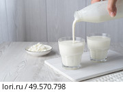 Pouring homemade kefir, buttermilk or yogurt with probiotics. Yogurt flowing from glass bottle on light background. Probiotic cold fermented dairy drink. Trendy food and drink. Copy space. Стоковое фото, фотограф Наталия Попова / Фотобанк Лори