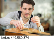 man changes guitar strings. Стоковое фото, агентство Ingram Publishing / Фотобанк Лори