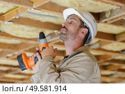 workman holding cordless drill looking up at roof timbers. Стоковое фото, агентство Ingram Publishing / Фотобанк Лори