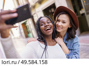 Two multiethnic women making selfie and grimacing with a smartphone.. Two beautiful multiethnic women making selfie and grimacing. Стоковое фото, агентство Ingram Publishing / Фотобанк Лори