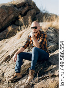 bald guy with a beard in jeans warm shirt and trekking shoes on granite rocks. Стоковое фото, агентство Ingram Publishing / Фотобанк Лори