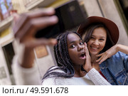 Two multiethnic women making selfie and grimacing with a smartphone.. Two beautiful multiethnic women making selfie and grimacing. Стоковое фото, агентство Ingram Publishing / Фотобанк Лори