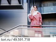 Young Muslim Woman walking on the street wearing hijab headscarf using smart phone in a office building. Business background.. Young Muslim woman wearing hijab using her smartphone. Стоковое фото, агентство Ingram Publishing / Фотобанк Лори