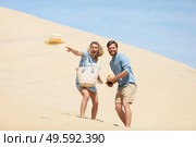 couple having fun on sand dune and throw hat forwards. Стоковое фото, агентство Ingram Publishing / Фотобанк Лори