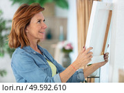 mature woman hanging picture on wall. Стоковое фото, агентство Ingram Publishing / Фотобанк Лори