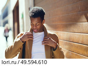 Young black man mending the collar of his coat in the street.. Black man mending the collar of his coat in the street. Стоковое фото, агентство Ingram Publishing / Фотобанк Лори