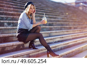 Blonde woman with beret, drinking a natural orange juice in a crystal glass, sitting on some urban steps.. Blonde woman with beret, drinking a natural orange juice in a crystal glass, sitting on some steps. Стоковое фото, агентство Ingram Publishing / Фотобанк Лори