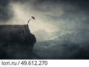 Fearless person on the edge of a cliff determined to catch his umbrella and fly away over abyss. Surreal adventure, conceptual scene for achievement and purposefulness. Стоковое фото, агентство Ingram Publishing / Фотобанк Лори